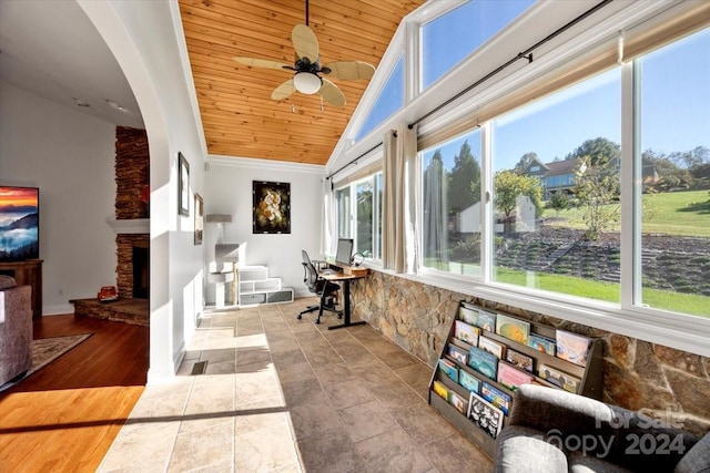 sunroom / solarium featuring a stone fireplace, ceiling fan, wooden ceiling, and vaulted ceiling