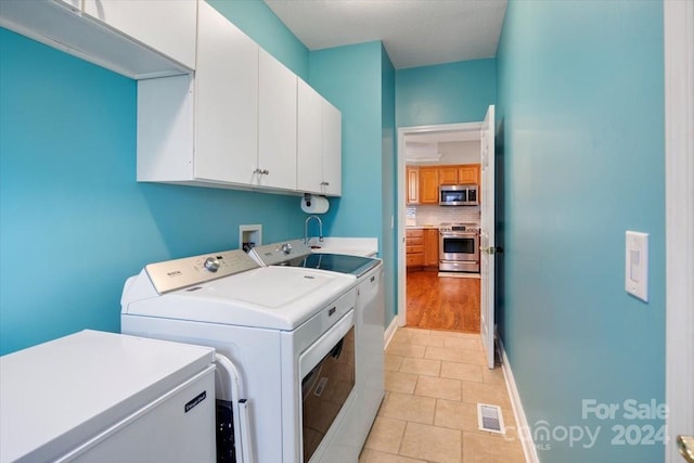 laundry room with cabinets, light tile patterned floors, and washing machine and clothes dryer