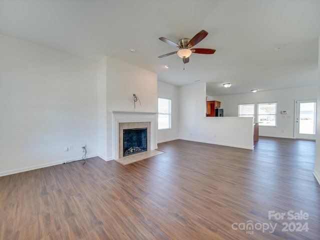 unfurnished living room featuring dark hardwood / wood-style floors, a tiled fireplace, and ceiling fan