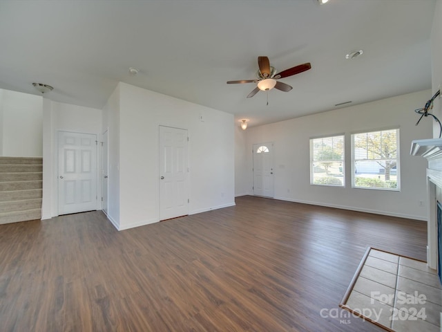 unfurnished living room featuring dark wood-style flooring, stairway, a fireplace, a ceiling fan, and baseboards