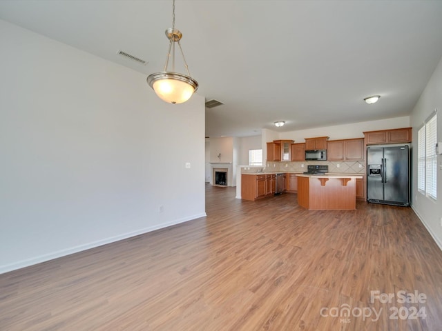 kitchen featuring decorative backsplash, a kitchen island, a kitchen breakfast bar, black appliances, and light wood-type flooring