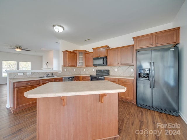 kitchen with glass insert cabinets, brown cabinetry, black appliances, a peninsula, and light countertops