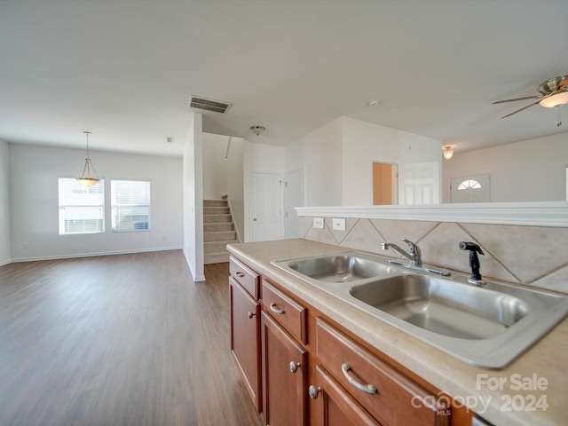 kitchen with sink, ceiling fan, pendant lighting, dark wood-type flooring, and a center island with sink