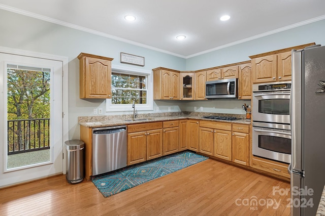 kitchen with appliances with stainless steel finishes, sink, light stone counters, light hardwood / wood-style floors, and crown molding