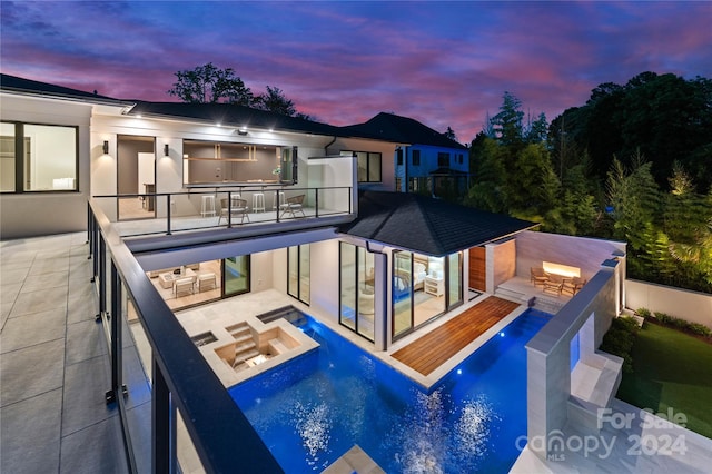 back house at dusk featuring a balcony, a patio, and a fenced in pool