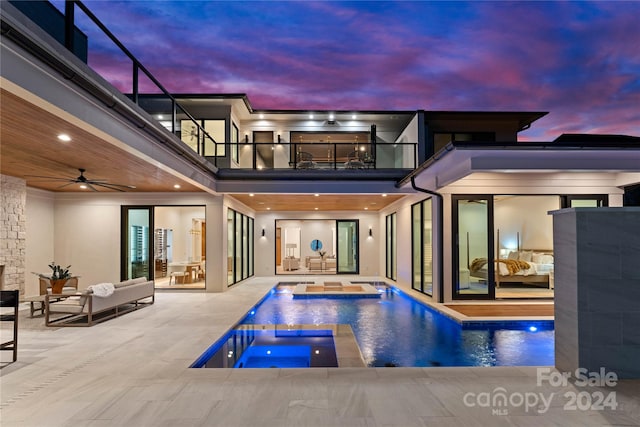 back house at dusk featuring a pool with hot tub, ceiling fan, a lanai, a patio area, and a balcony