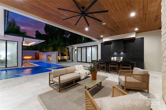 pool at dusk featuring an outdoor kitchen, outdoor lounge area, a patio, and ceiling fan