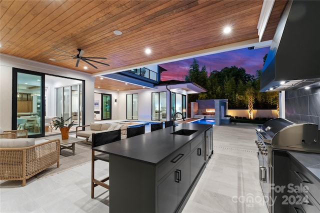 patio terrace at dusk with a pool, an outdoor kitchen, an outdoor hangout area, sink, and ceiling fan