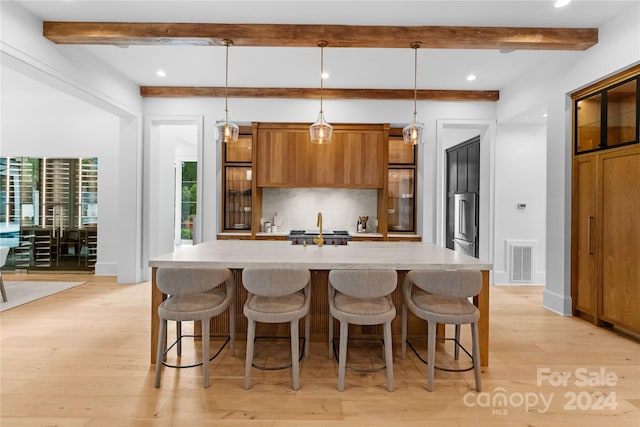 kitchen with decorative backsplash, beamed ceiling, an island with sink, decorative light fixtures, and light hardwood / wood-style floors