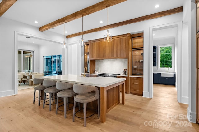 kitchen featuring tasteful backsplash, pendant lighting, beam ceiling, light hardwood / wood-style flooring, and a center island with sink