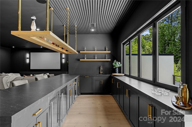 bar with custom range hood, light hardwood / wood-style flooring, dark stone counters, and sink