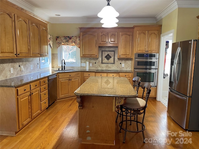 kitchen with appliances with stainless steel finishes, light wood-type flooring, a center island, sink, and decorative light fixtures