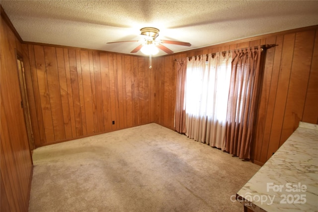 unfurnished room featuring carpet floors, a ceiling fan, a textured ceiling, and wooden walls