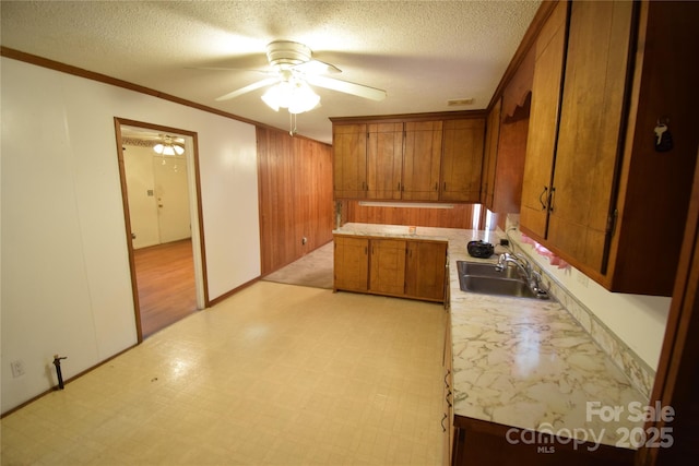 kitchen featuring crown molding, ceiling fan, light countertops, brown cabinets, and a sink