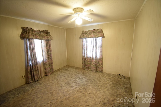 carpeted spare room featuring wooden walls, ceiling fan, and crown molding
