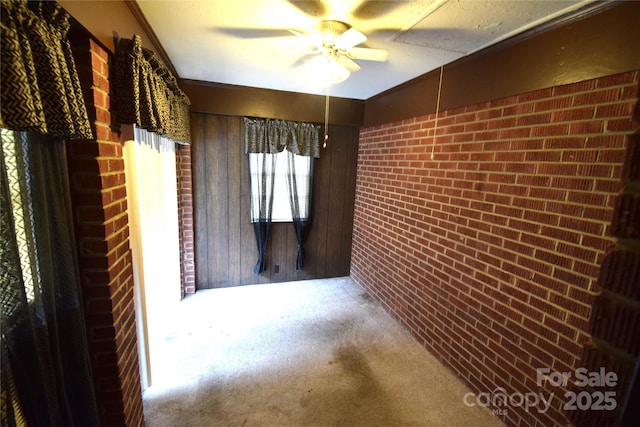 carpeted spare room featuring crown molding, ceiling fan, wood walls, and brick wall