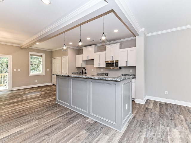 kitchen featuring beamed ceiling, crown molding, white cabinetry, and an island with sink