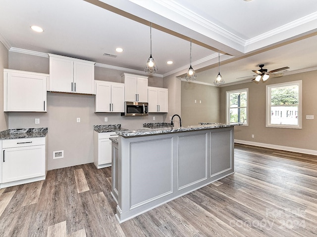 kitchen with white cabinets, a center island with sink, hardwood / wood-style flooring, and ornamental molding