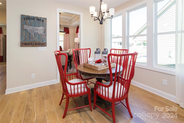 dining area with a healthy amount of sunlight, a raised ceiling, a chandelier, and hardwood / wood-style floors