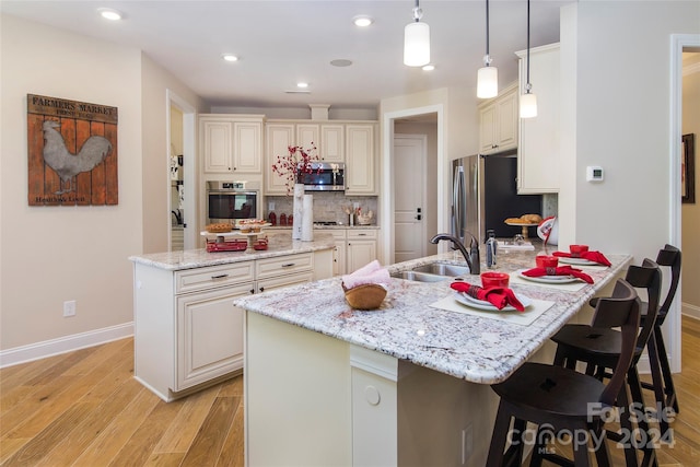 kitchen featuring light stone countertops, appliances with stainless steel finishes, an island with sink, light hardwood / wood-style floors, and pendant lighting