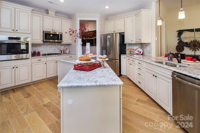 kitchen with sink, appliances with stainless steel finishes, light hardwood / wood-style flooring, and pendant lighting