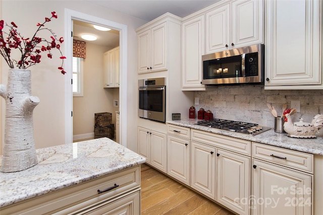 kitchen featuring light stone counters, stainless steel appliances, light wood-type flooring, and backsplash