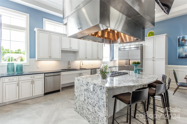 kitchen featuring wall chimney range hood, white cabinets, backsplash, stainless steel appliances, and a center island