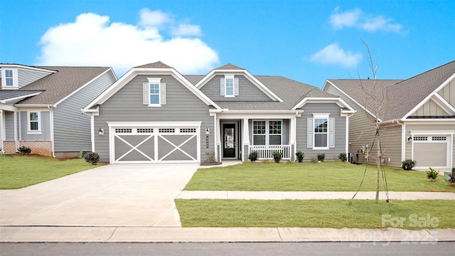 craftsman-style house featuring concrete driveway, roof with shingles, an attached garage, covered porch, and a front lawn