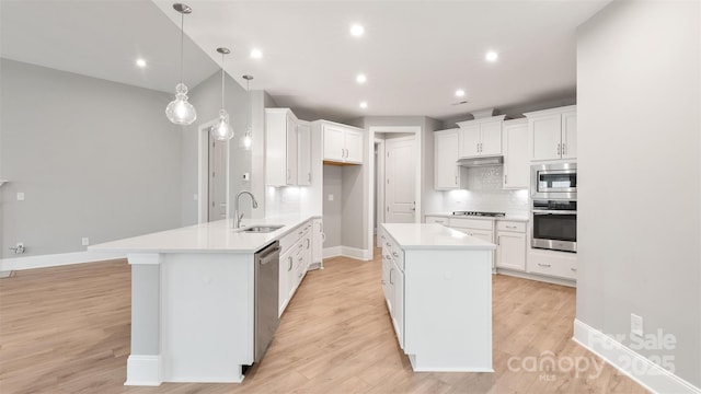 kitchen featuring decorative light fixtures, stainless steel appliances, light countertops, white cabinetry, and a sink