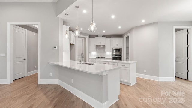 kitchen featuring appliances with stainless steel finishes, decorative light fixtures, light countertops, white cabinetry, and a sink