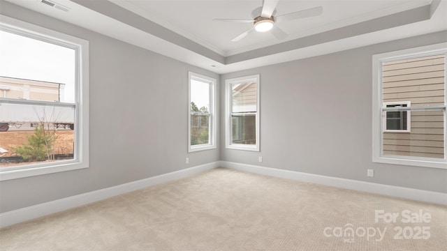 empty room with baseboards, visible vents, a tray ceiling, and light colored carpet