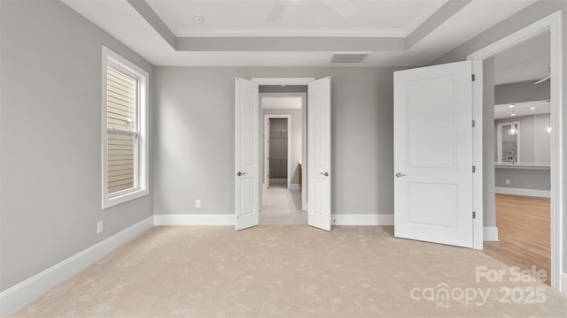 unfurnished bedroom with a tray ceiling, visible vents, and baseboards