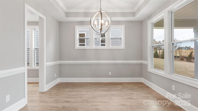 unfurnished dining area with a chandelier, a raised ceiling, and light wood-style floors