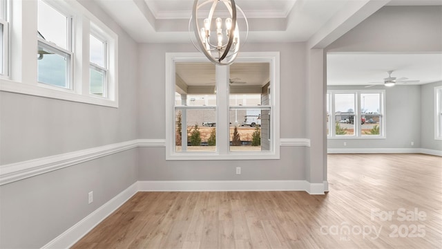 unfurnished dining area featuring crown molding, light wood finished floors, a raised ceiling, and baseboards