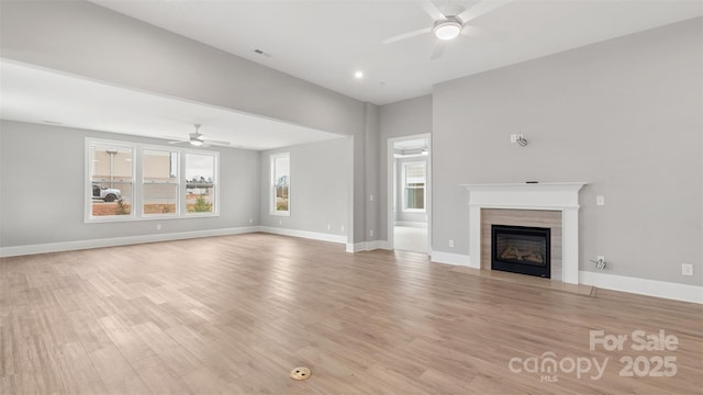 unfurnished living room featuring ceiling fan, light wood finished floors, a tile fireplace, and baseboards