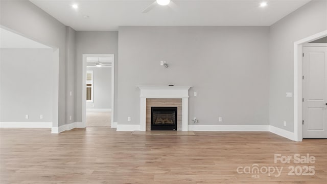 unfurnished living room with a tiled fireplace, light wood-type flooring, a ceiling fan, and baseboards