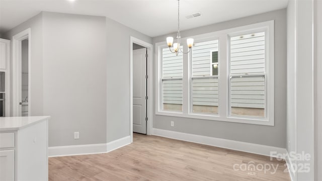 unfurnished dining area with visible vents, an inviting chandelier, light wood-style flooring, and baseboards