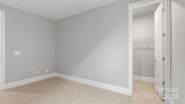 unfurnished bedroom with baseboards, a spacious closet, a closet, and light colored carpet