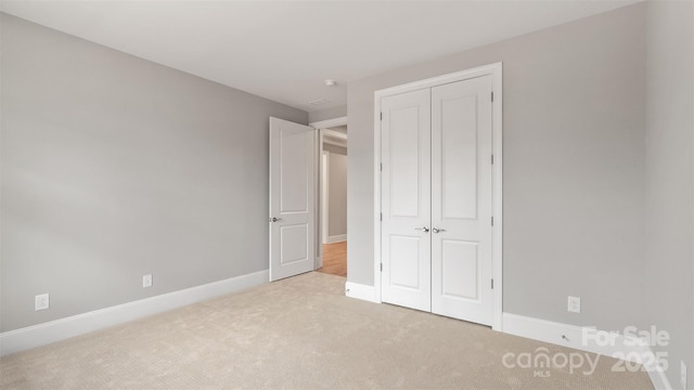 unfurnished bedroom with baseboards, a closet, and light colored carpet