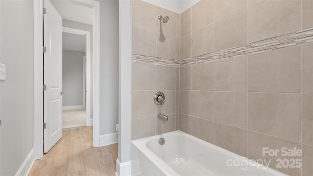 bathroom featuring toilet, baseboards, shower / washtub combination, and wood finished floors