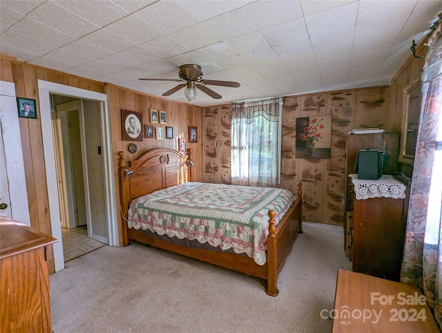 bedroom with ceiling fan, wood walls, and light colored carpet