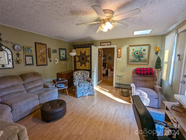 living room featuring a skylight, a textured ceiling, ceiling fan, ornamental molding, and light hardwood / wood-style flooring