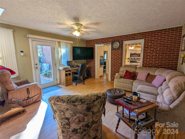 living room with light hardwood / wood-style floors, brick wall, a textured ceiling, and ceiling fan