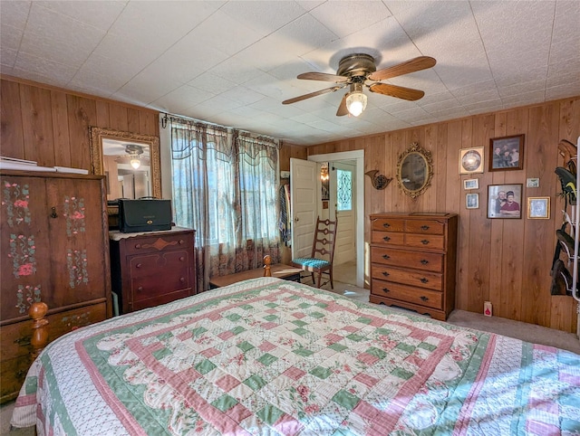 carpeted bedroom featuring wood walls and ceiling fan