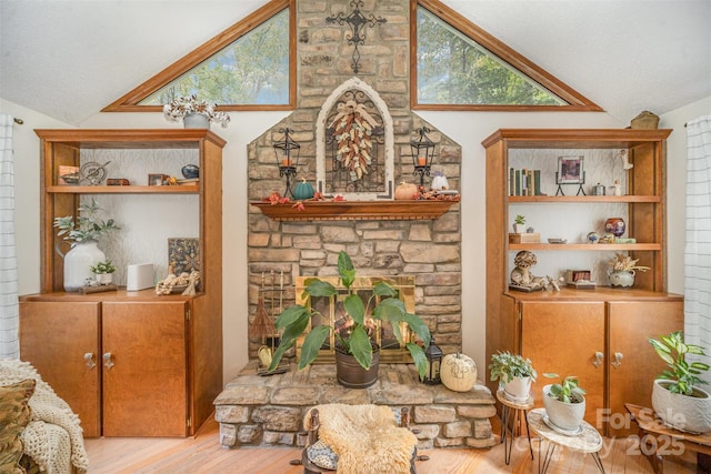 interior space featuring lofted ceiling, a stone fireplace, light hardwood / wood-style flooring, and a textured ceiling