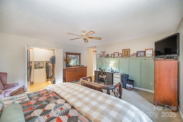 carpeted bedroom with ceiling fan, a walk in closet, a textured ceiling, and a closet