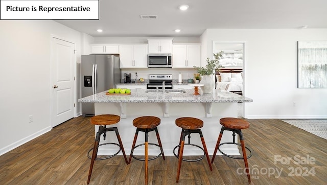 kitchen featuring dark wood-type flooring, appliances with stainless steel finishes, white cabinetry, and an island with sink