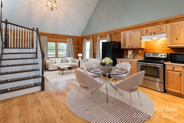 kitchen featuring black appliances, light wood-type flooring, high vaulted ceiling, and wood walls