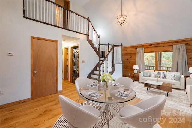 dining room featuring light hardwood / wood-style floors, wood walls, stacked washer / drying machine, and high vaulted ceiling