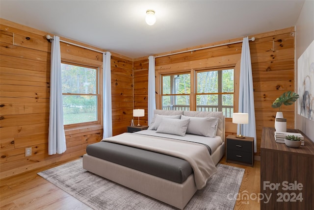 bedroom featuring wooden walls, multiple windows, and wood-type flooring